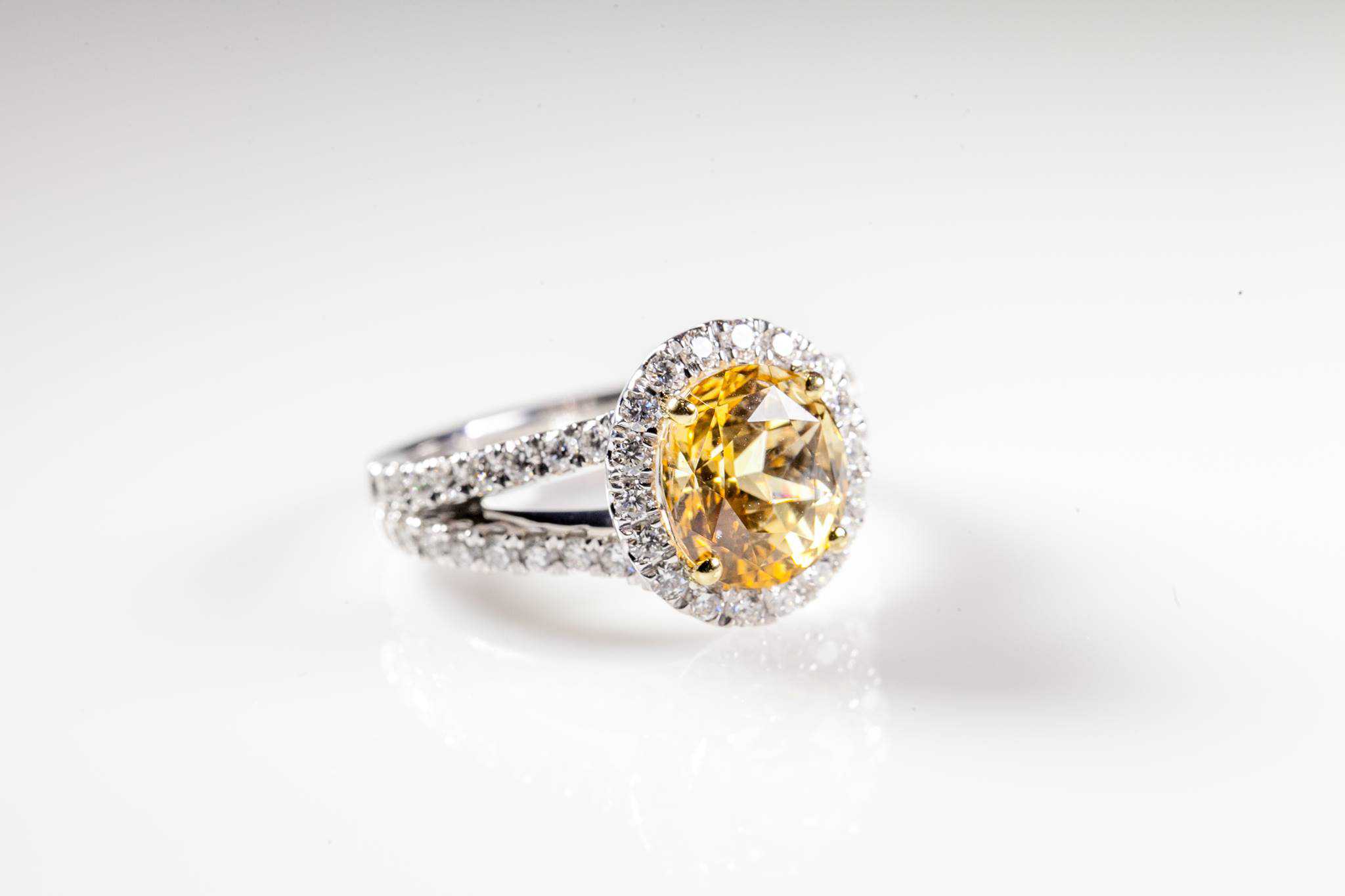 Silver ring with a large round yellow gemstone surrounded by small clear diamonds on a white background.